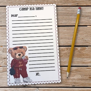 May include: A notepad with the text "CAMP Tea Time!" and a cartoon bear wearing sunglasses and a maroon tracksuit. A yellow pencil with a pink eraser rests on a wooden surface.