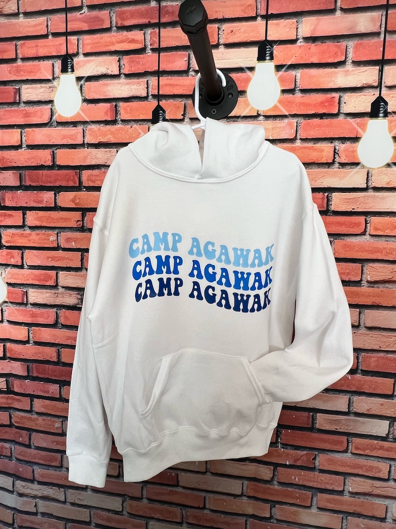 May include: White hooded sweatshirt with a blue and white graphic that says "Camp Agawak" in a retro font.