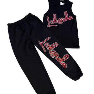 Puede incluir: Camiseta sin mangas y pantalones de ch&aacute;ndal negros con un gr&aacute;fico "Lokanda" degradado rojo y naranja en la parte delantera y la pierna.