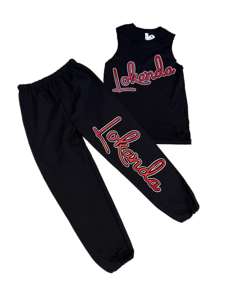 Puede incluir: Camiseta sin mangas y pantalones de ch&aacute;ndal negros con un gr&aacute;fico "Lokanda" degradado rojo y naranja en la parte delantera y la pierna.