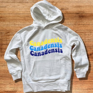 May include: White hooded sweatshirt with the word "Canadensis" repeated three times in a retro font, with each word in a different color: yellow, blue, and navy blue.