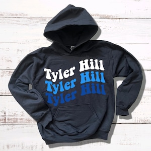 May include: A dark blue hooded sweatshirt with the text "Tyler Hill" repeated three times in a gradient of blue and white.