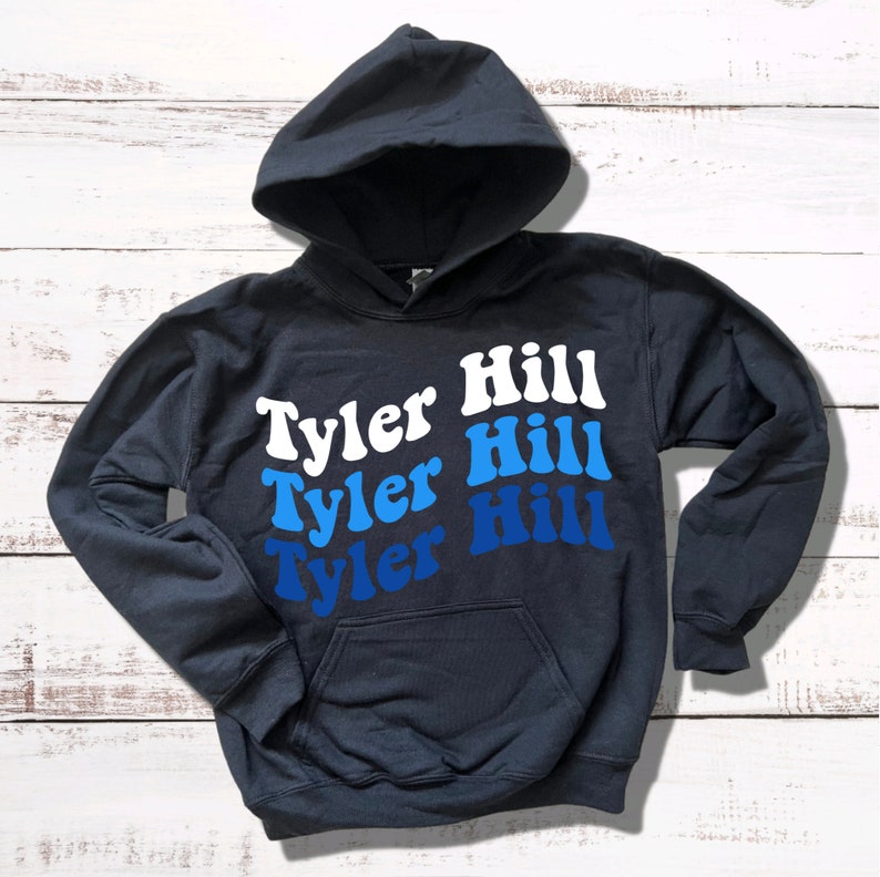 May include: A dark blue hooded sweatshirt with the text "Tyler Hill" repeated three times in a gradient of blue and white.