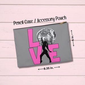 May include: Gray pencil case or accessory pouch with a gold zipper. The design features the word "LOVE" in pink, with a black silhouette of a person holding a disco ball. The pouch is approximately 8.35 inches wide and 6 inches tall.