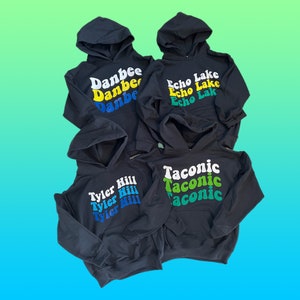 May include: Four black hooded sweatshirts with different colored text on the front. The text on the sweatshirts reads "Danbee", "Echo Lake", "Tyler Hill", and "Taconic".