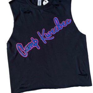 Puede incluir: Camiseta negra sin mangas con detalles desgastados. La camiseta presenta un gr&aacute;fico rosa y azul que dice "Camp Kweebec".