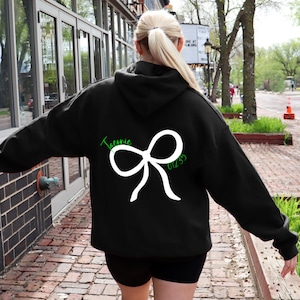 May include: Black hooded sweatshirt with a white bow and the text "Ticonic 01235" in green on the back.