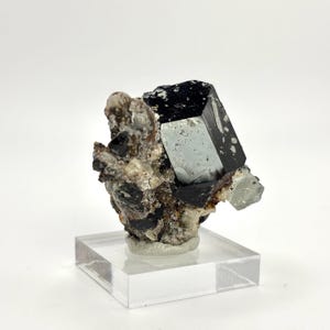 以下が含まれることがあります： 大きなファセットクリスタルを備えた黒とグレーの鉱物標本。鉱物は透明なアクリルディスプレイスタンドに置かれています。標本は、より小さな結晶を持つ粗くテクスチャード加工されたマトリックスを持っています。