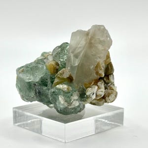 May include: A natural crystal cluster, with a prominent clear quartz formation and green fluorite. The crystals are interspersed with golden and white mineral deposits. The specimen is presented on a clear acrylic stand, highlighting its natural form.