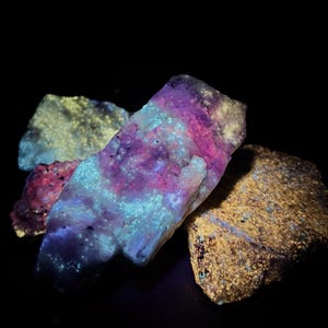 May include: A collection of glowing mineral specimens, showcasing a range of colours. The rocks exhibit purple, pink, blue, and yellow hues, set against a black backdrop. The image highlights the natural textures and formations of the minerals.