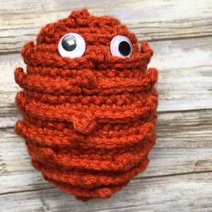 May include: A crocheted orange-brown monster with large white googly eyes.