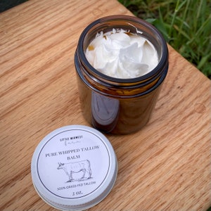 Peut inclure: Un pot en verre avec un couvercle blanc contenant un baume fouett&eacute; blanc. Le couvercle porte une &eacute;tiquette noire et blanche qui indique "LITTLE MIDWEST farm PURE WHIPPED TALLOW BALM 100% GRASS-FED TALLOW 2 OZ."