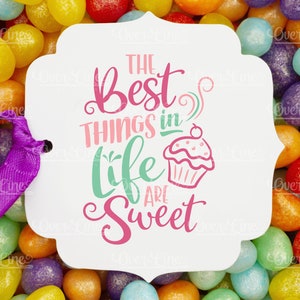 May include: A white card with the text "THE BEST THINGS in life ARE Sweet" in pink and green, with a cupcake illustration. The card is attached to a purple ribbon and set against a colorful background of jelly beans.