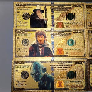May include: Gold-colored $100 bills featuring characters from The Lord of the Rings. The bills have images of Gandalf, Frodo, and Gollum. The bills are labeled "GOLD 999999" and "FEDERAL RESERVE NOTE".
