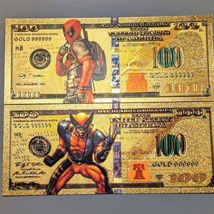 May include: Two gold-colored novelty $100 bills featuring illustrations of Deadpool and Wolverine. The bills have the text "GOLD 999999" and "100" printed on them. The background has a glittery texture.