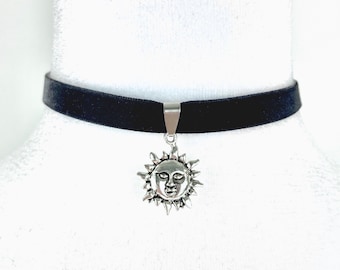 May include: A black velvet choker necklace with a silver sun pendant. The sun pendant has a face and a spiky halo.