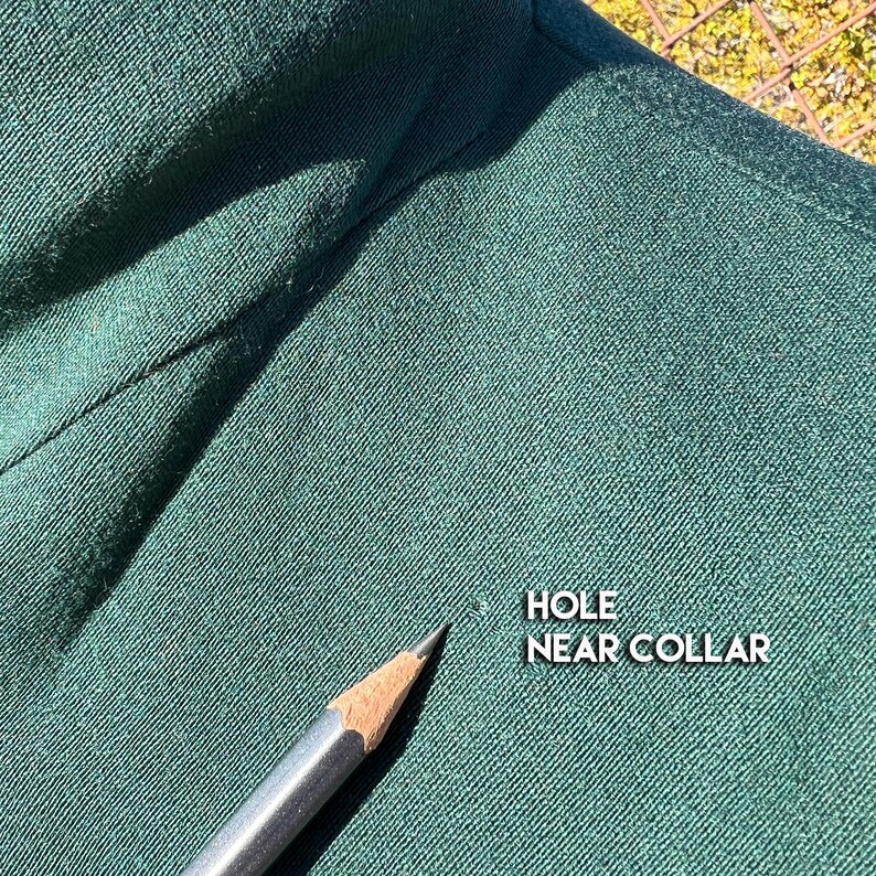 May include: Close-up of dark green fabric with a pencil pointing to a small hole near the collar. The text "HOLE NEAR COLLAR" is visible in white. The fabric appears to be a woven material.