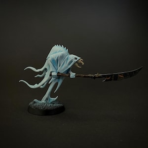 Puede incluir: Una figura fantasmal con una cara esquelética y una túnica blanca que fluye sostiene una lanza de hoja negra. La figura está pintada de azul claro y está de pie sobre una base negra.