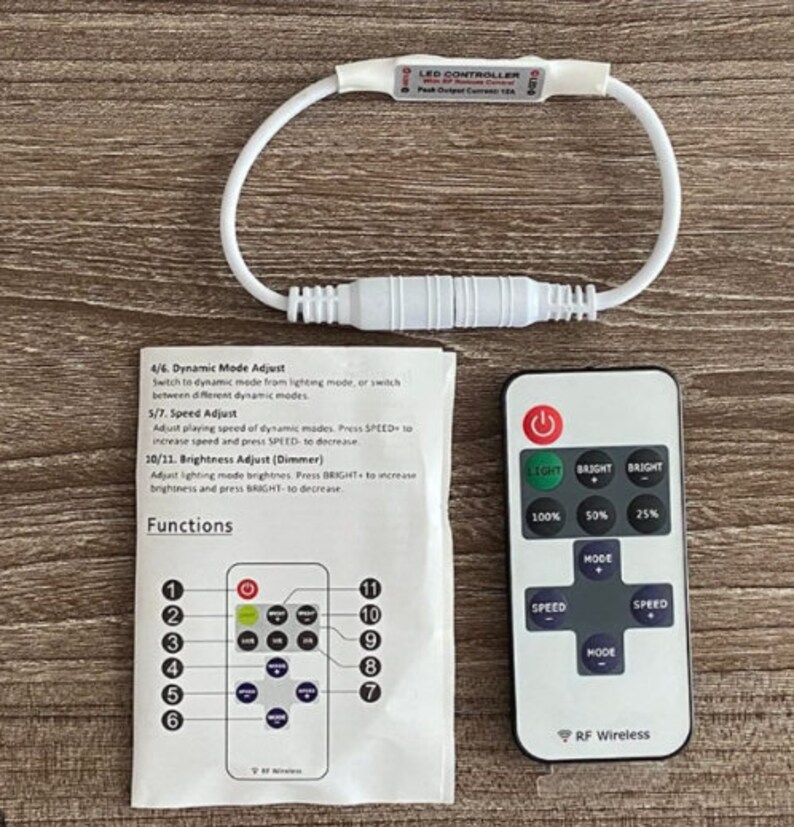 May include: A white LED controller with a remote control. The controller has a white wire loop and a connector. The remote control has buttons for light, mode, and speed. The text on the controller reads "LED CONTROLLER with RF Remote Control Peak Output Current 15A". The text on the remote control reads "RF Wireless".