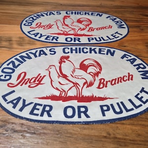 May include: Two oval-shaped patches with a chicken farm theme. The patches feature a red rooster and hen illustration on a white background, with text in blue and red. The text reads "GOZINYA'S CHICKEN FARM Indy Branch LAYER OR PULLET."