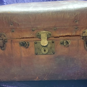 May include: A vintage brown leather suitcase with brass hardware and a lock. The suitcase has a rounded top and is in good condition.