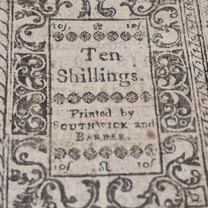 May include: Close-up of a vintage document with ornate borders. The text reads "Ten Shillings" and "Printed by SOUTHWICK and BARBER." The document has a faded, aged appearance, with decorative floral and scroll elements.