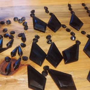 May include: A collection of black crystal teardrop and diamond-shaped chandelier prisms. The prisms are arranged on a wooden surface.