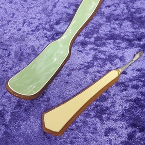 May include: Two vintage plastic handled tools. One is a green and brown spatula with a rounded tip. The other is a cream and brown tool with a pointed tip and a small metal blade.