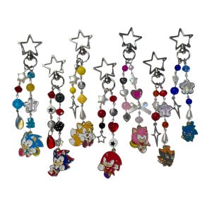 May include: A collection of beaded keychains featuring various Sonic the Hedgehog characters. Each keychain has a star-shaped clasp and a dangling design with colorful beads, charms, and a character pendant.