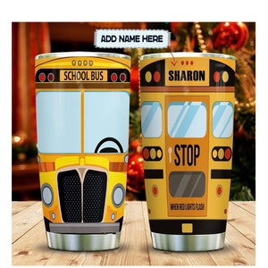Può includere: Un bicchiere in acciaio inossidabile a tema scuolabus giallo con un coperchio nero. Il bicchiere presenta un'immagine di uno scuolabus sul davanti e le parole "SCHOOL BUS" in alto. Il retro del bicchiere ha un'immagine di uno scuolabus con le parole "SHARON" in alto e "STOP" in basso. Il bicchiere è su una superficie di legno.