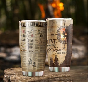May include: Two stainless steel tumblers with a vintage design. One tumbler features a compass with the text "Live your life by a compass not a clock". The other tumbler features a vintage illustration of hiking tips and a hiking backpack.