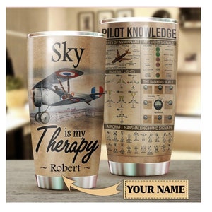 Może przedstawiać: Kubek ze stali nierdzewnej z grafiką vintage samolotu i tekstem "Sky is my Therapy ~ Robert ~". Druga strona kubka zawiera wykres wiedzy pilota z informacjami o częściach samolotu, sygnałach świetlnych ATC, światłach pasa startowego i sygnałach ręcznych kierowania statkiem powietrznym.