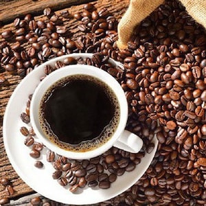 May include: A white coffee cup filled with dark coffee sits on a white saucer, surrounded by roasted coffee beans. A burlap sack spills more coffee beans onto a rustic wooden surface, creating a warm, inviting scene.