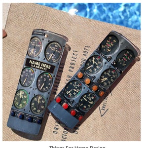 May include: Two gray metal can coolers with a vintage airplane cockpit instrument panel design. The can coolers feature various gauges, dials, and labels, including "NAME HERE" and "U.S. AIRWAYS".
