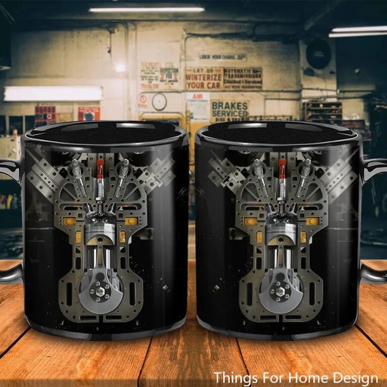 May include: Two black ceramic mugs featuring a detailed image of a car engine printed on them. The mugs are on a wooden surface.