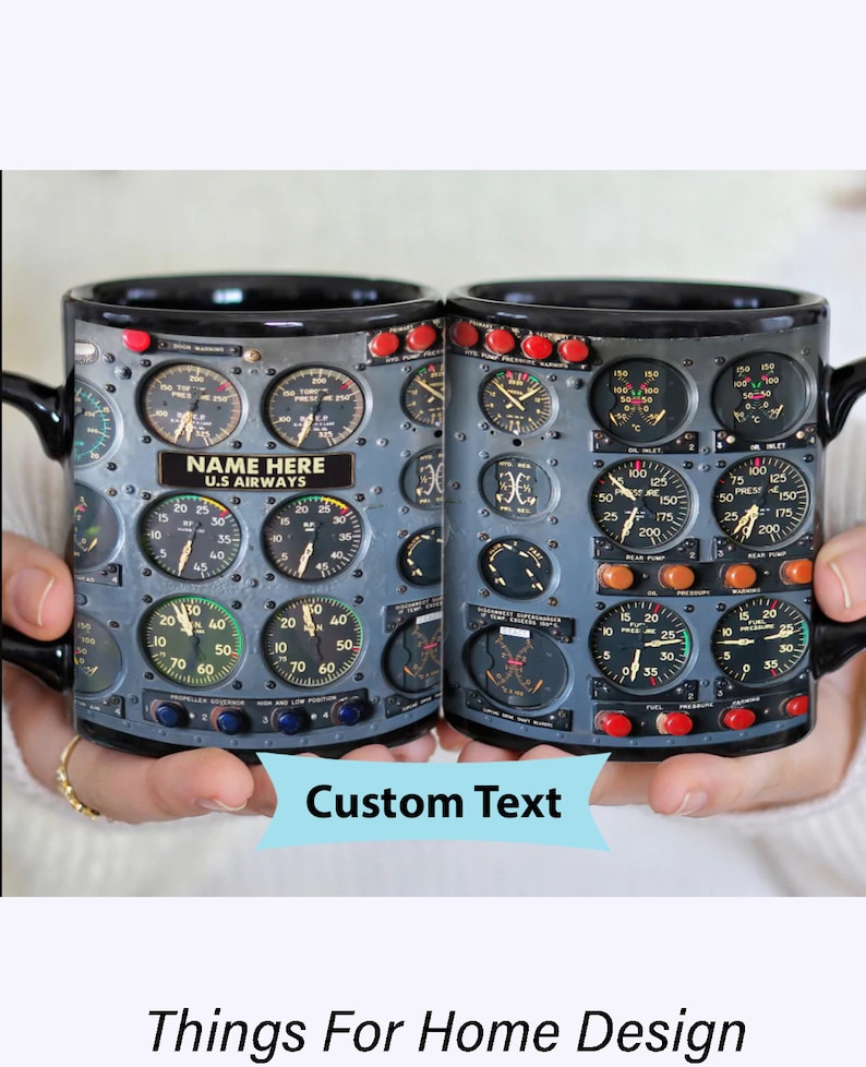 May include: A black ceramic mug with a design of an airplane cockpit instrument panel. The panel features various gauges and dials with numbers and labels. The mug has a handle and the text "NAME HERE U.S. AIRWAYS" is printed on the panel.