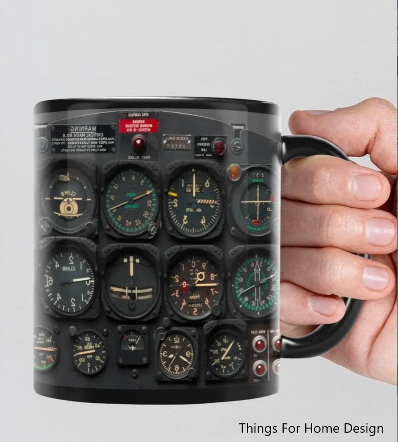 May include: Black ceramic mug with a design of a vintage airplane cockpit instrument panel. The panel features multiple round gauges with black and white markings and red and green needles. The mug has a black handle.