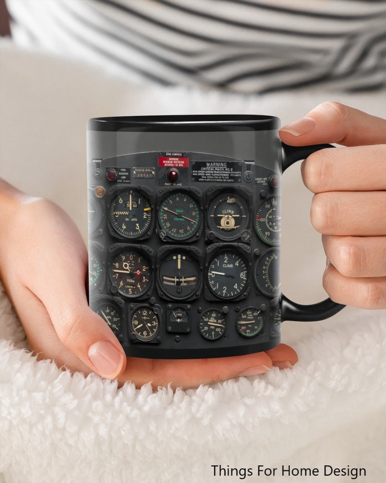 May include: Black coffee mug with a design of an airplane cockpit instrument panel. The panel features various gauges and dials, including a compass, altitude indicator, and airspeed indicator. The text "WARNING CRITICAL MACH No.1" is visible on the panel.