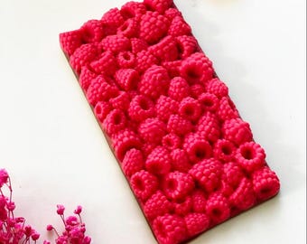May include: A chocolate bar with a raspberry design. The bar is made of dark chocolate and is covered in a layer of pink raspberry-shaped candies.