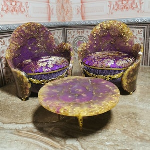 May include: Two purple and gold chairs with ornate details and a matching purple and gold round table. The chairs have a floral pattern on the seat cushions.