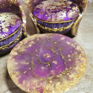 May include: A purple and gold resin table with a swirling pattern and gold flakes. The table is round and has a smooth, glossy finish.