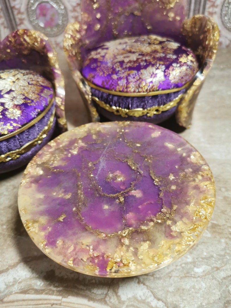 May include: A purple and gold resin table with a swirling pattern and gold flakes. The table is round and has a smooth, glossy finish.
