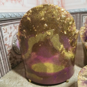 May include: A small, decorative chair made of resin with a purple and gold marbled finish. The chair has a rounded back and gold accents.