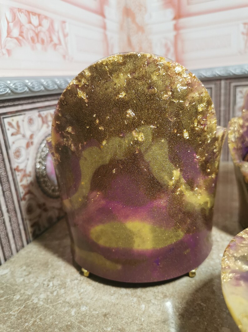 May include: A small, decorative chair made of resin with a purple and gold marbled finish. The chair has a rounded back and gold accents.