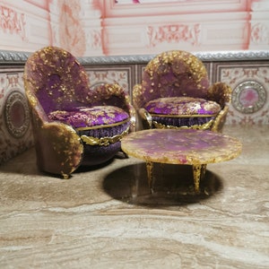 May include: Two purple and gold chairs with ornate details and a matching purple and gold round table with a resin top.