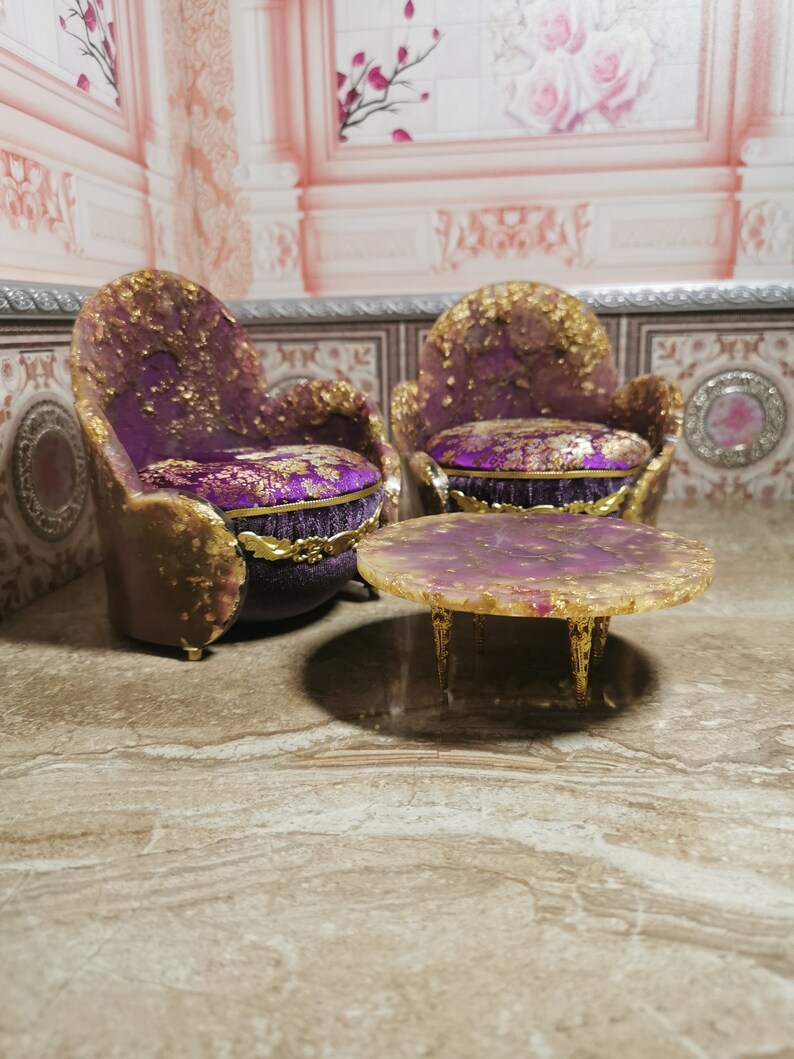 May include: Two purple and gold chairs with ornate details and a matching purple and gold round table with a resin top.
