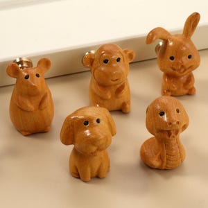 May include: A selection of wooden animal-shaped cabinet knobs. The knobs feature a mouse, monkey, rabbit, dog, and snake. Each knob is light brown with black eyes and a brass screw fitting.