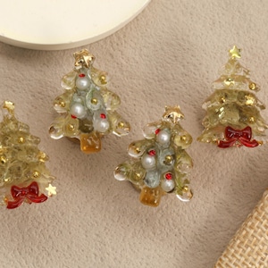Könnte beinhalten: Vier Miniatur-Weihnachtsbaum-Ornamente. Jeder Baum ist eine durchscheinende Goldfarbe mit Perlen- und roten Perlenakzenten, einem goldenen Stern oben und einer roten Schleife an der Basis. Die Ornamente befinden sich auf einem neutralen Hintergrund.