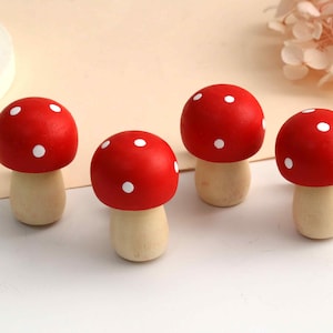 May include: Four small mushroom figurines crafted from wood. Each piece features a rounded, bright red cap painted with small white polka dots and a smooth, light beige cylindrical stem. The set is arranged in a group on a flat surface.