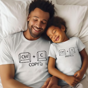 May include: White t-shirts with a computer keyboard design. The father's shirt says "Ctrl + C COPY" and the child's shirt says "Ctrl + V PASTE".